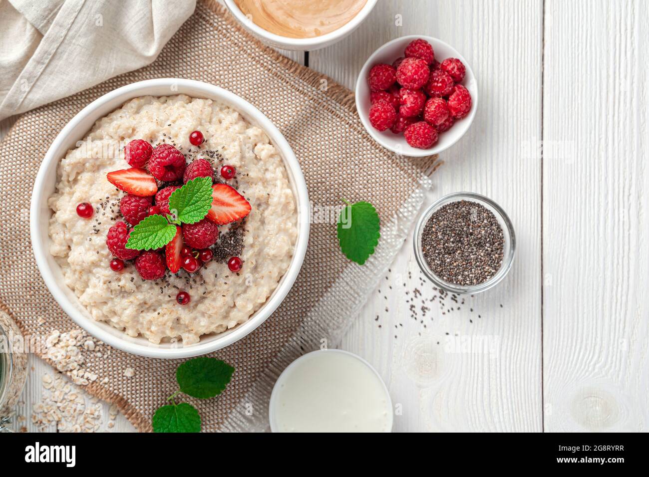Oatmeal porridge with fresh berries, chia seeds and mint on a light background. Top view, copy space. Stock Photo
