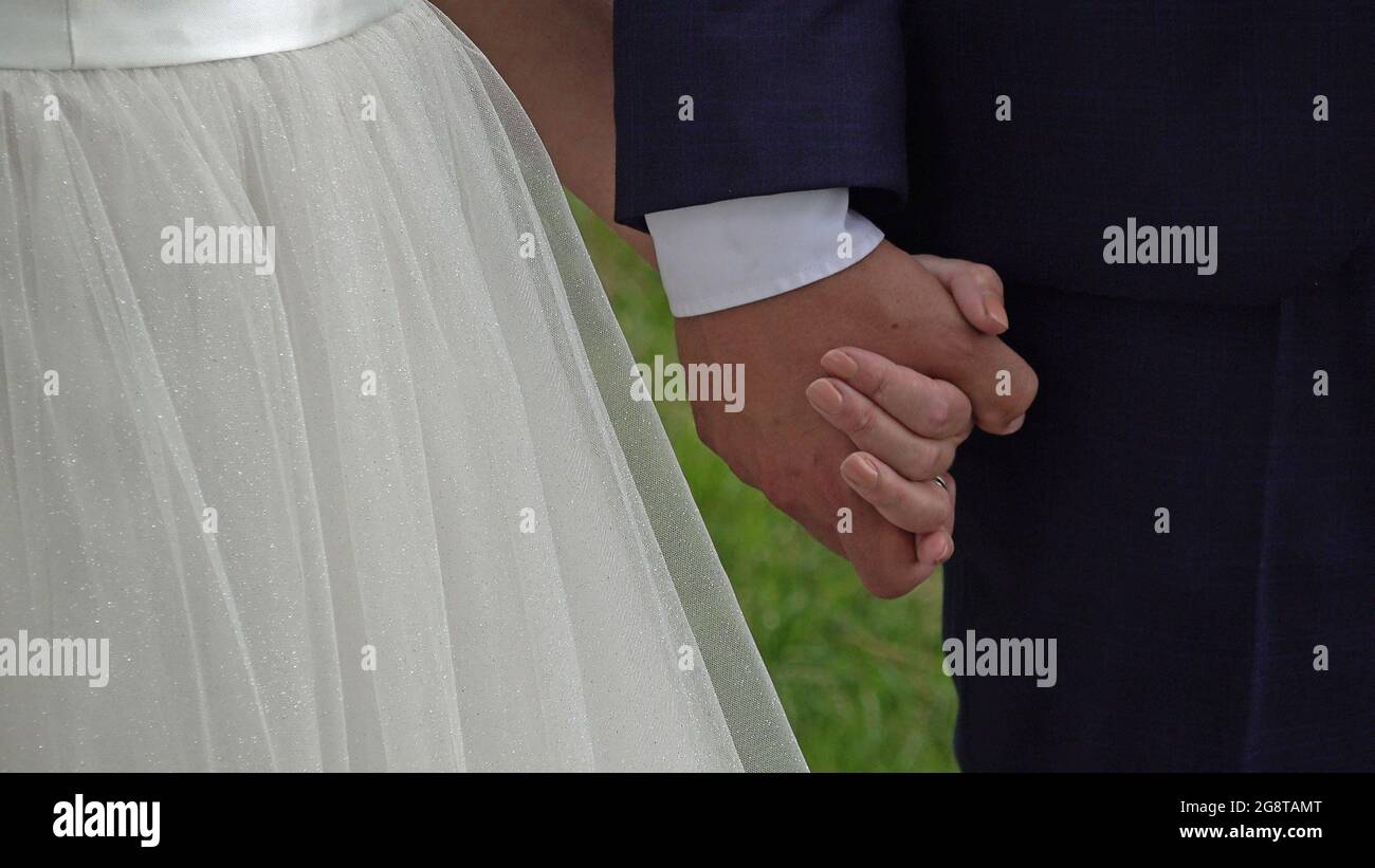Close-up of bride and groom hands. The bride has a white dress and the groom a blue suit. Stock Photo