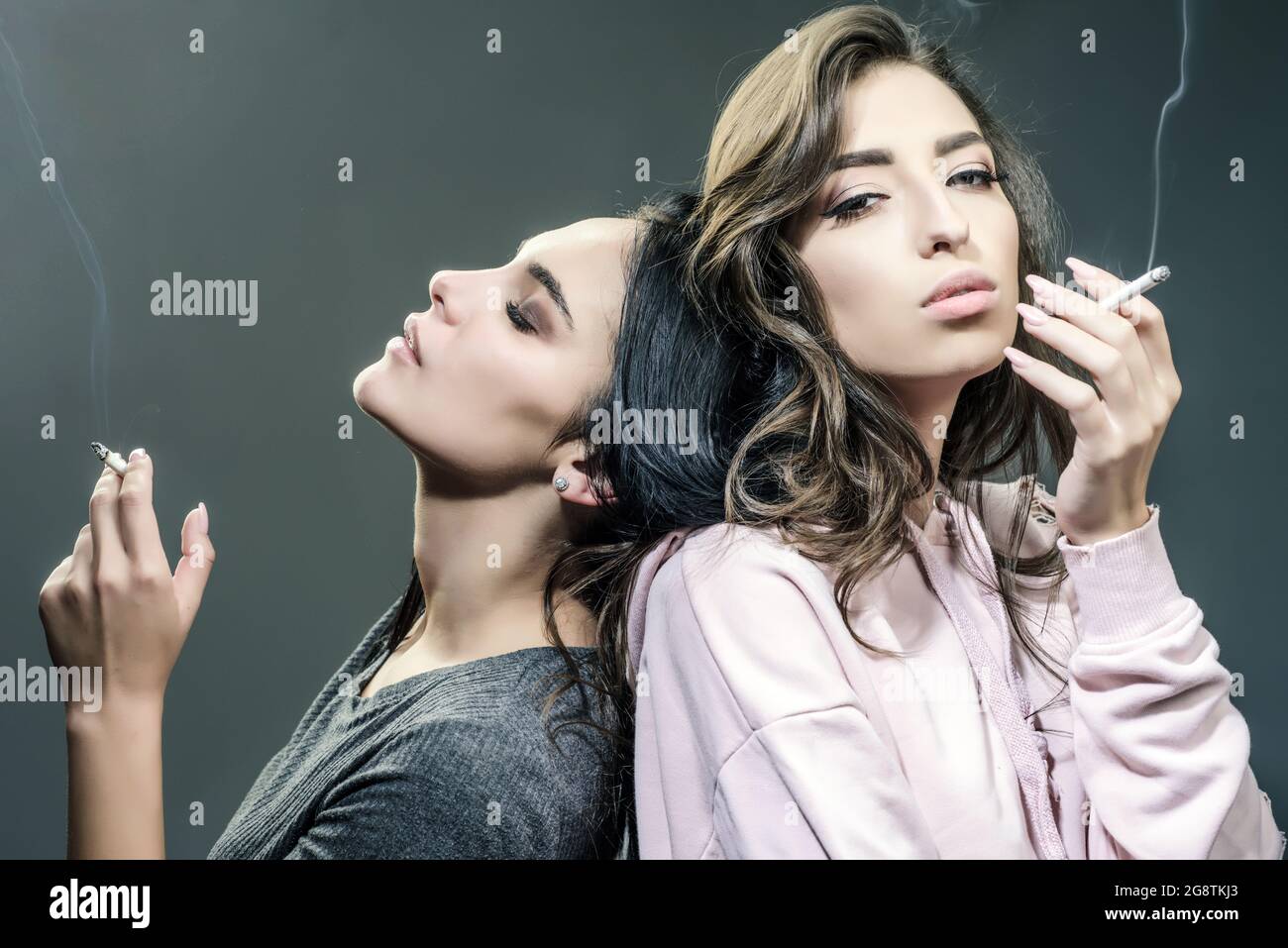 Smoking addiction. Actual social problem. Drug addict or medical abuse concept. Two sad woman with depression Smoking on the gray Background Stock Photo