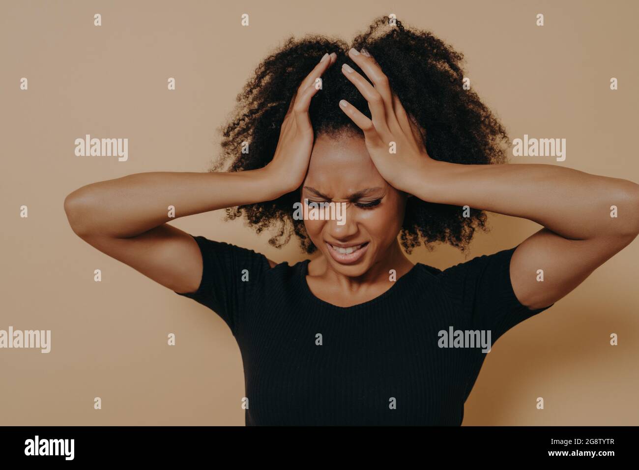 Stressful young african woman keeping head with hands with closed eyes and suffering from headache Stock Photo