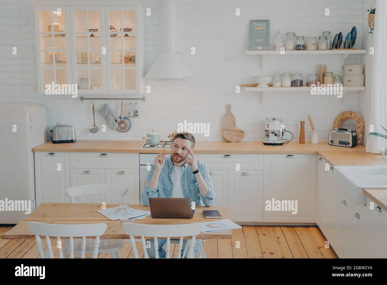 Young office worker working remotely from home with computer while sitting by kitchen table Stock Photo