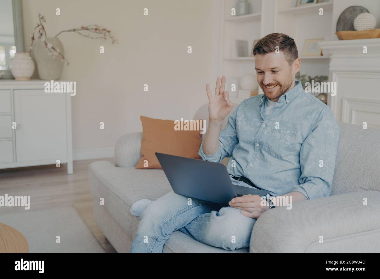 Young office male worker showing okay gesture while in online meeting at home Stock Photo