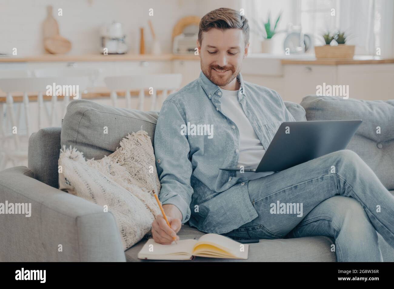 Young office worker working remotely from home researching using notebook and taking notes Stock Photo