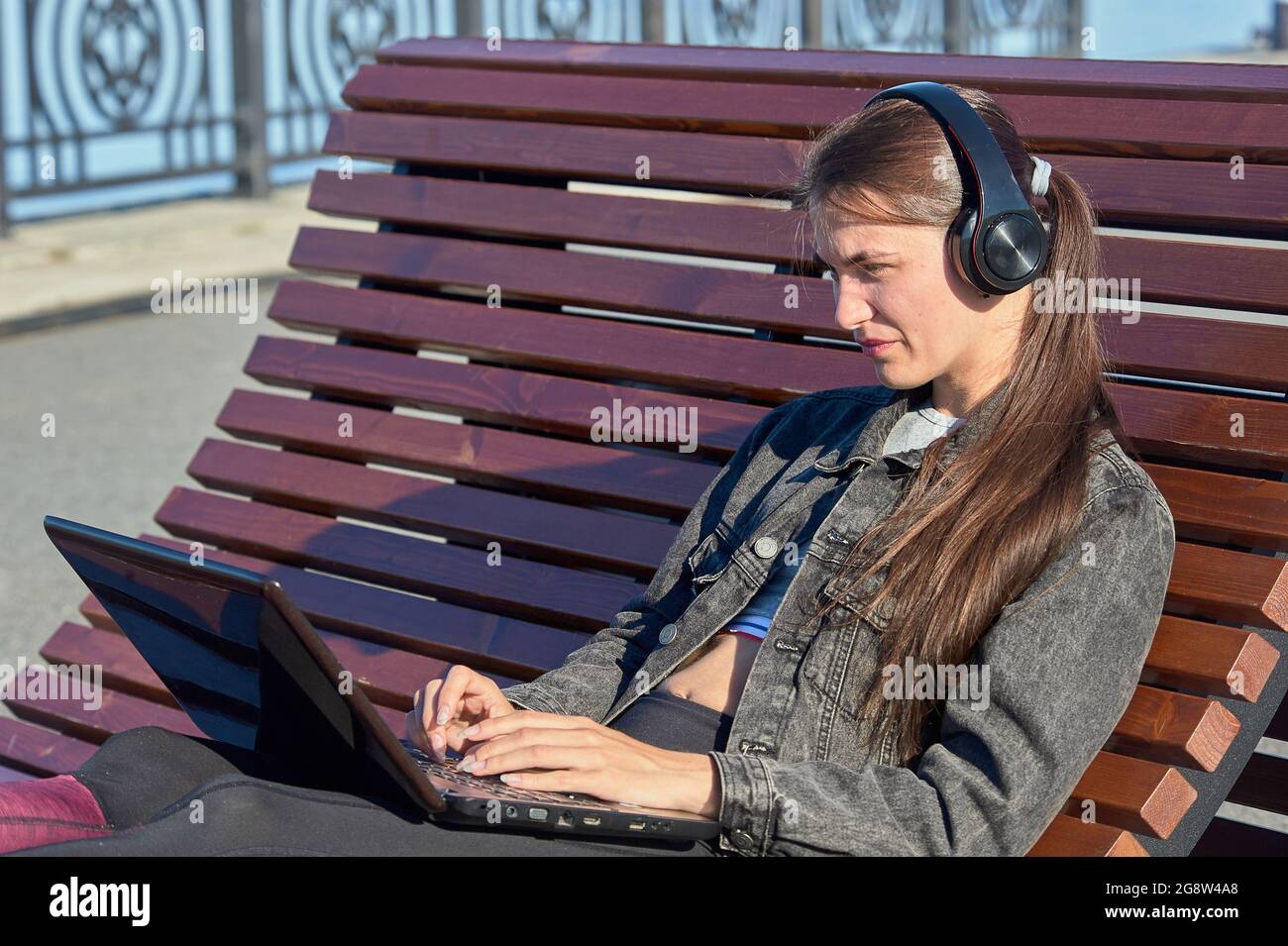 A woman with a laptop sits on an outdoor bench and works online Stock Photo