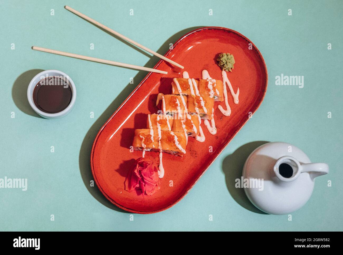 Sushi roll with soy sauce and chopsticks on a wooden stand on a bright yellow-blue background. Sushi menu. Japanese cuisine. Stock Photo