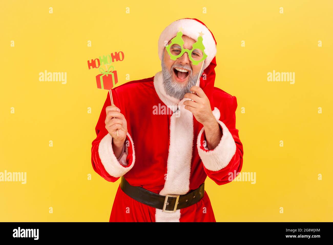 Excited elderly man with gray beard wearing santa claus costume holding congratulations cards on sticks, new year and christmas celebration. Indoor st Stock Photo