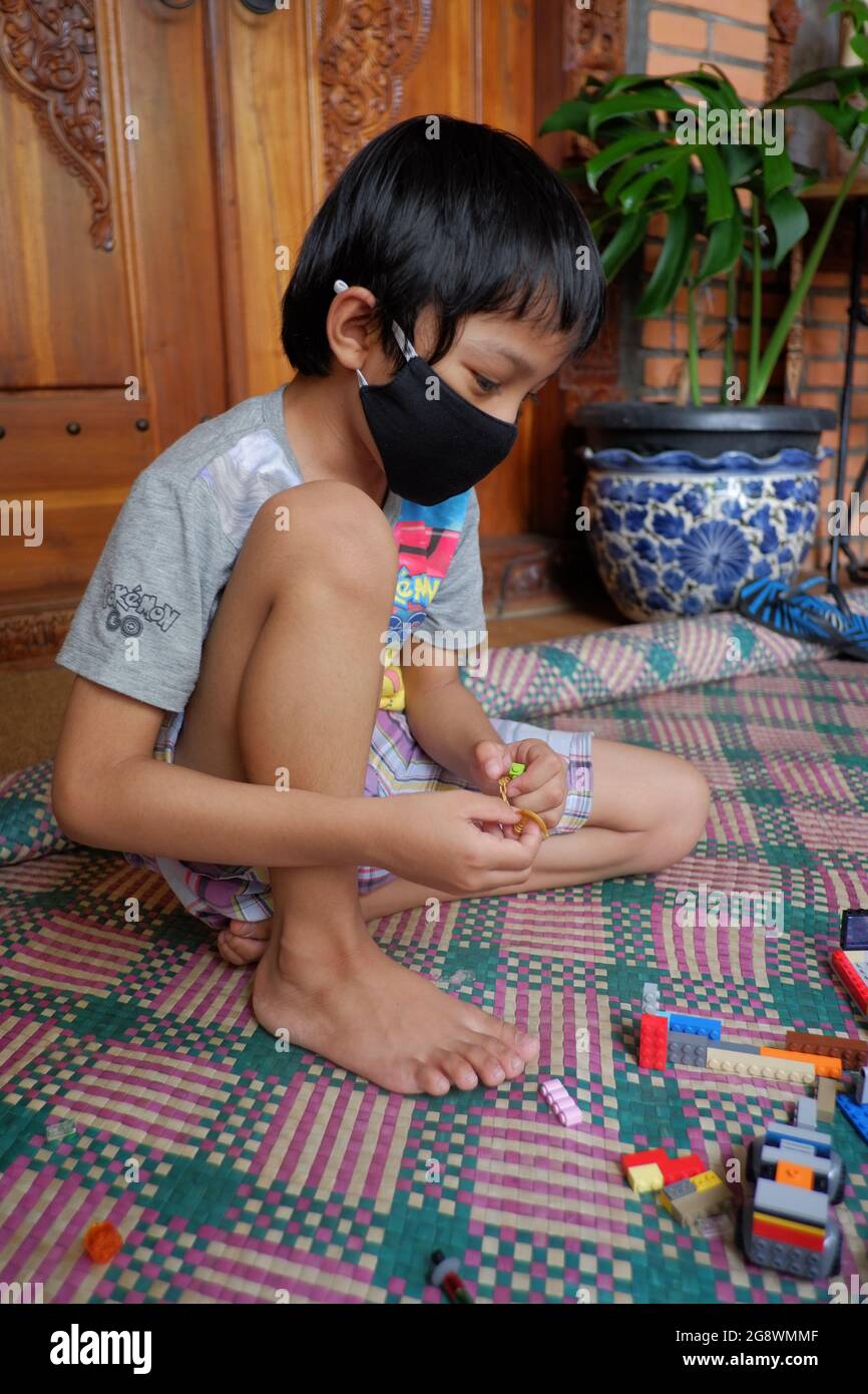 A boy with facemask plays lego toys in his house. Stock Photo