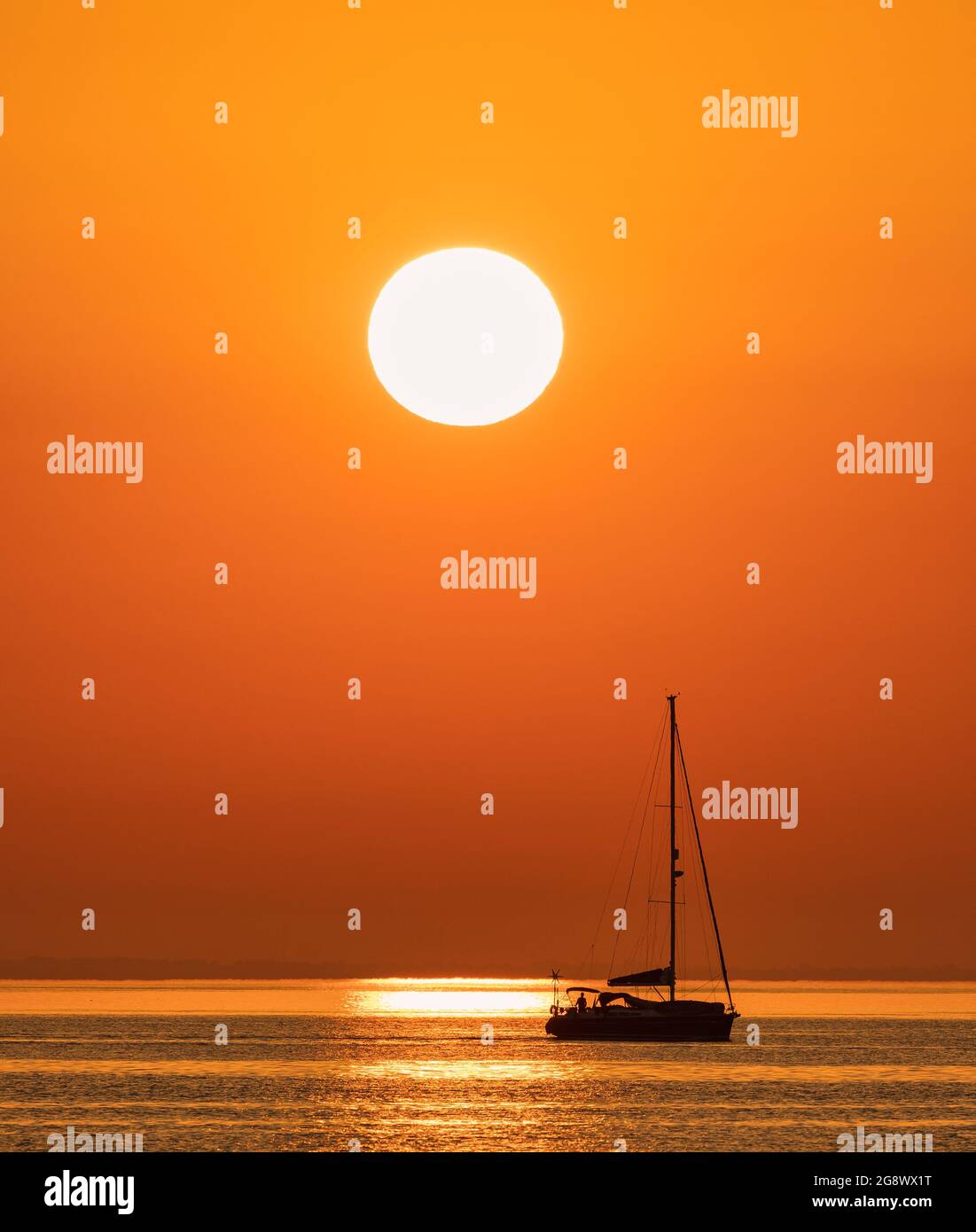 A small yacht leaves Swanage marina and heads out into the English Channel with the sun rising in the East Stock Photo