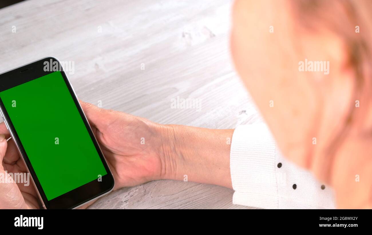 Middle-aged female senora uses an iPhone smartphone with a chroma key screen, copy space. Online shopping concept, use of mobile applications: Moscow Stock Photo