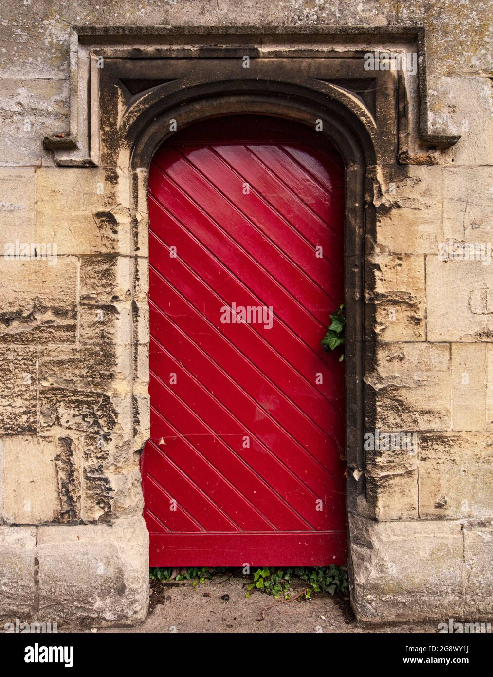 Old red door in wall of house in Banbury Road, Oxford with decorative lintel or architrave typical of Oxford architecture; warm golden stone of wall Stock Photo