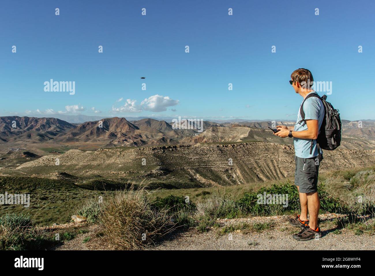 Man playing with drone for exam. Silhouette against mountain landscape.Male operating the drone by remote control and having fun. Pilot flying drone. Stock Photo