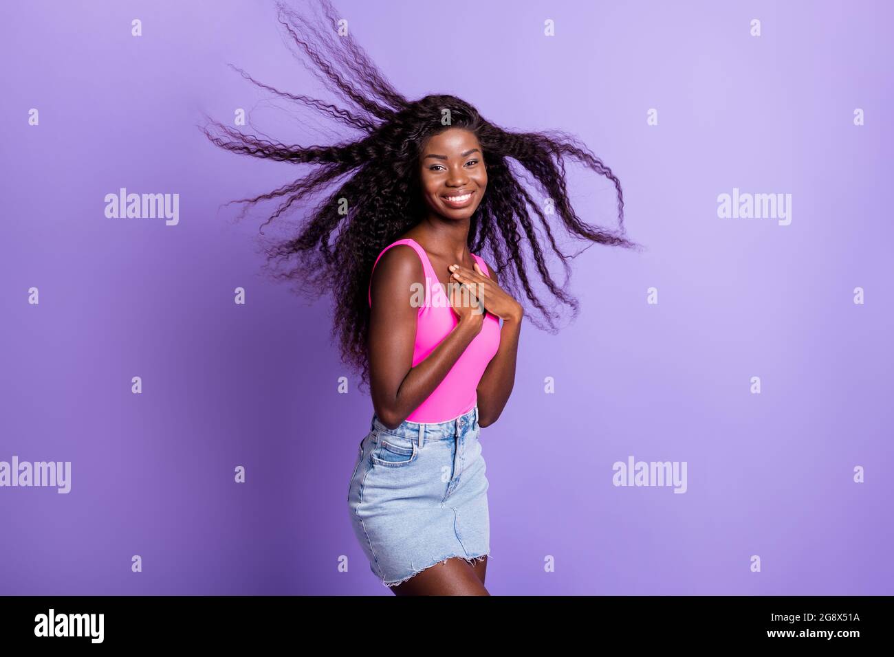 Photo portrait of african american woman with flying hair touching chest isolated on pastel pink colored background Stock Photo
