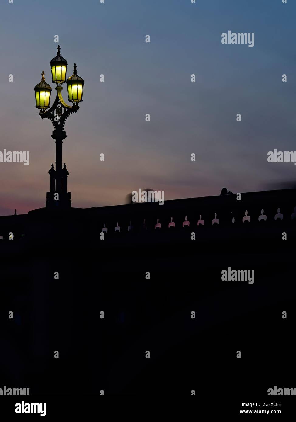 Low-key, soft view looking up to the parapet of Westminster Bridge where a gothic streetlight stands and some people move in motion-blurred silhouette. Stock Photo