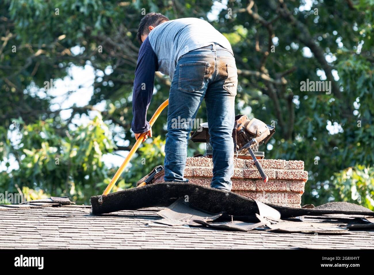 A contractor standing on a residential roof removing shingles to put a