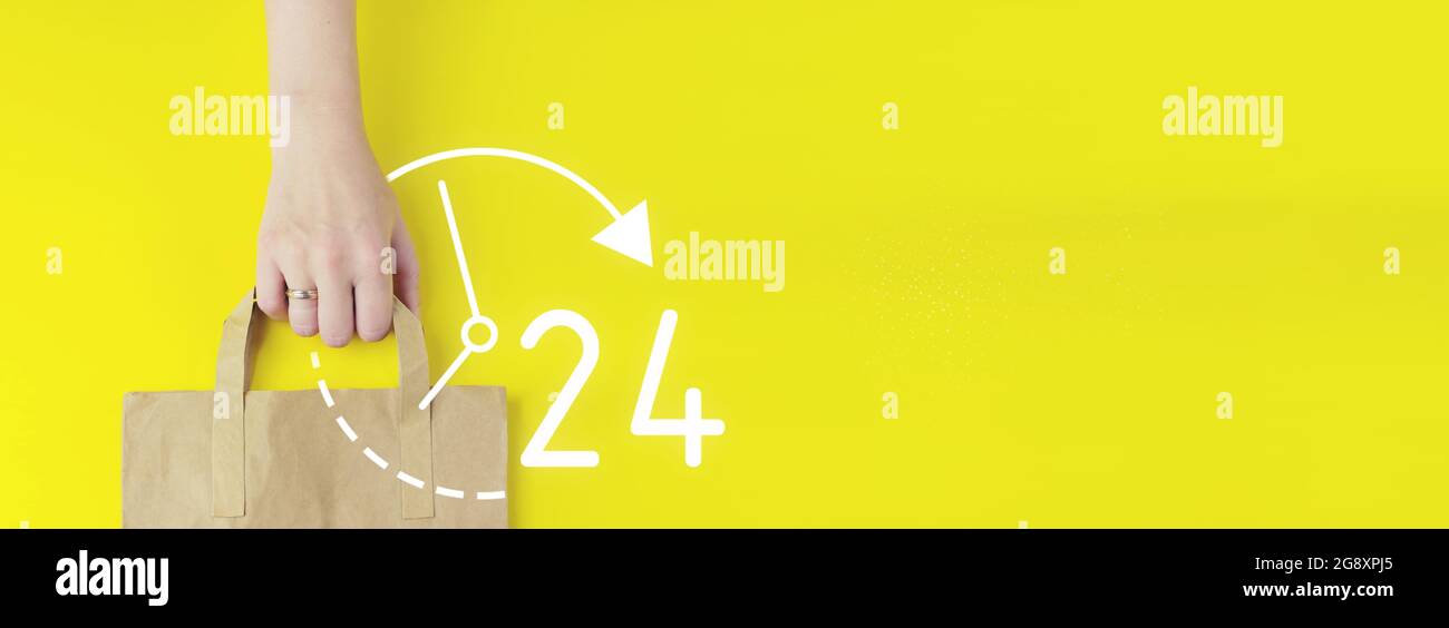 Full time service concept. Recycled brown paper shopping bag in hand with hologram 24 7 all day all night icon on yellow background, flat lay. Summer Stock Photo