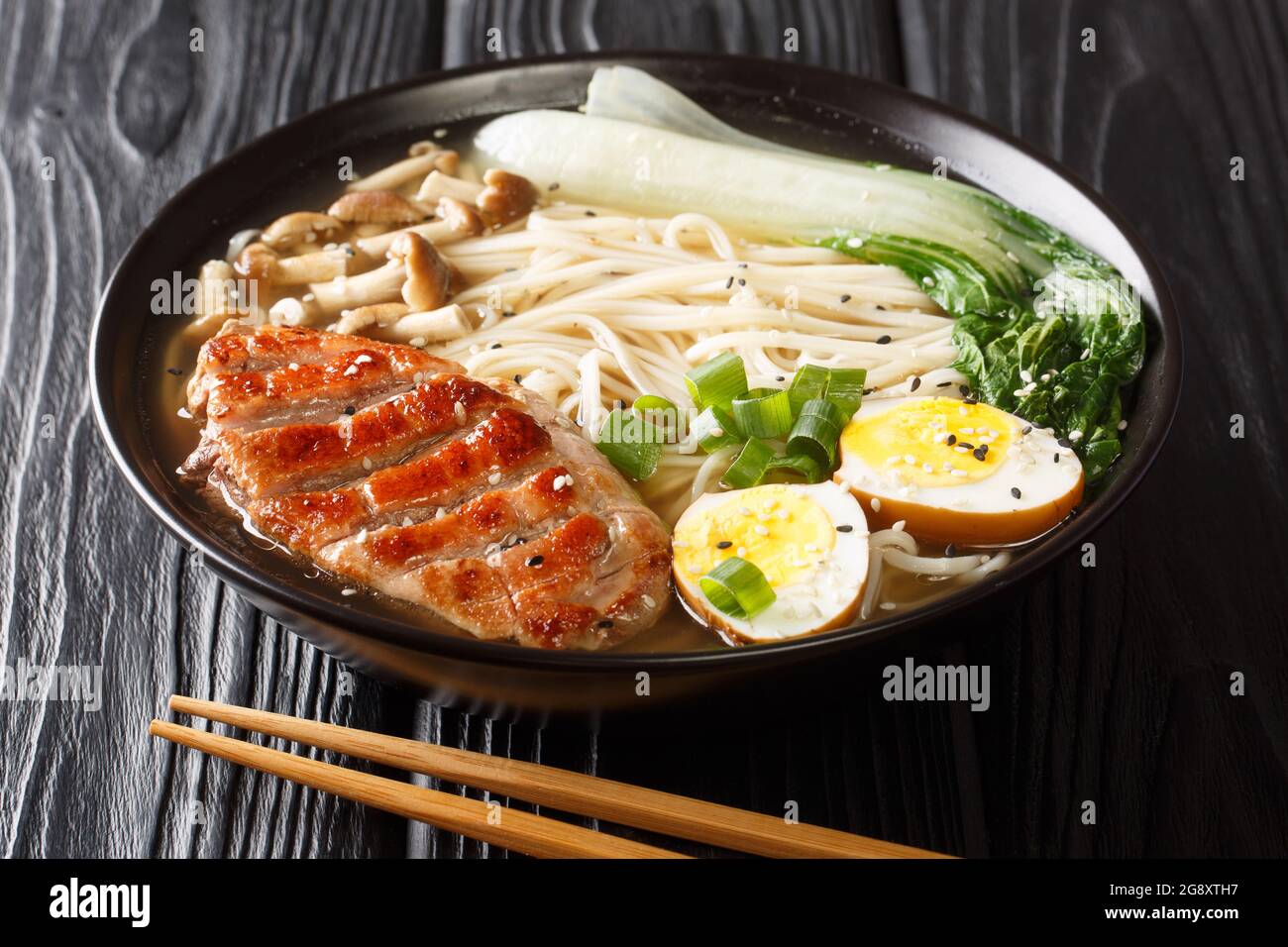Asian noodle soup, ramen with duck, mushroom, vegetables and egg in bowl on black wooden background. horizontal Stock Photo
