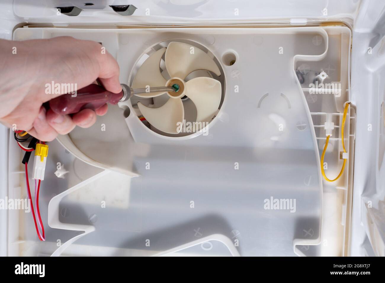 A technician uses a screwdriver in refrigerator fridge. Inside refrigerator repair. Disassembled refrigerator. Removed back cover fridge. fan repair. Stock Photo
