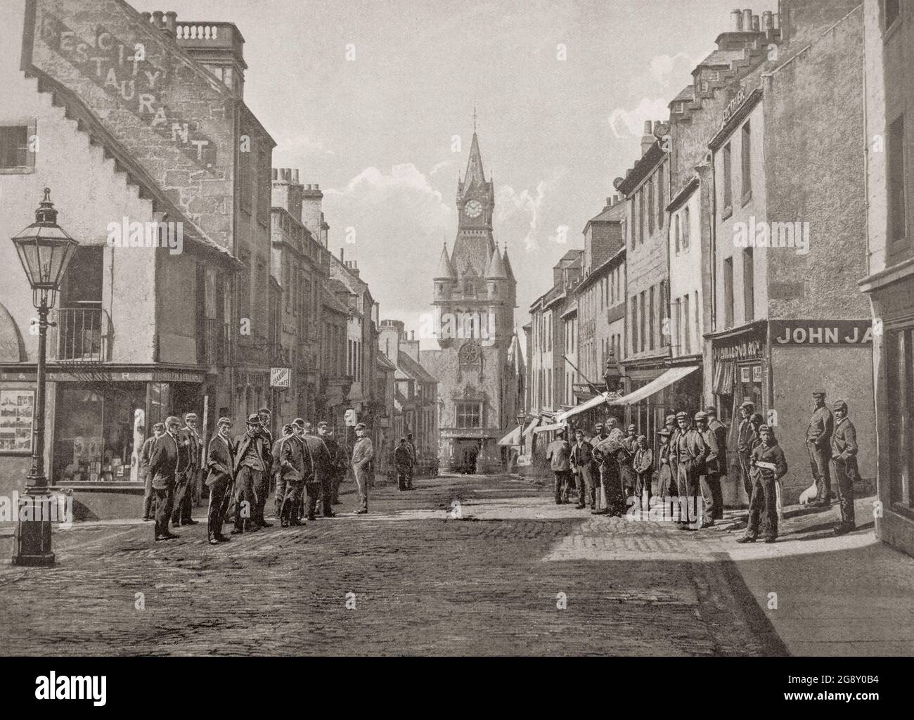 A late 19th century view of the High Street in Dunfermline, a town and former Royal Burgh in Fife, Scotland. At the end of the crowded street is Dunfermline City Chambers, designed by James Campbell Walker in the French Gothic style, and completed in May 1879. It was built to replace the old town house after rapid industrial growth in the local area. Stock Photo