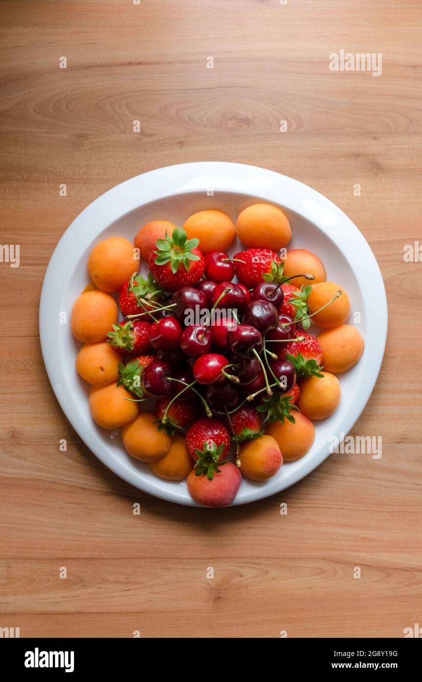 Friuts on a white plate with cherries, strawberries and mirabelle plums Stock Photo