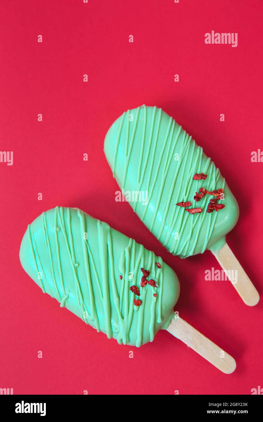 cake - popsicle in green glaze on a red background. space for text. Ice cream sweet eskimo with chocolate icing. Chocolate covered ice cream on stick Stock Photo