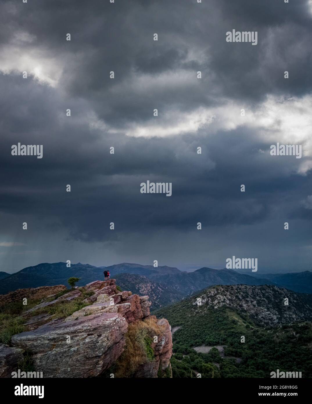Dark storm and unrecognizable hikers on top of the rocks Stock Photo
