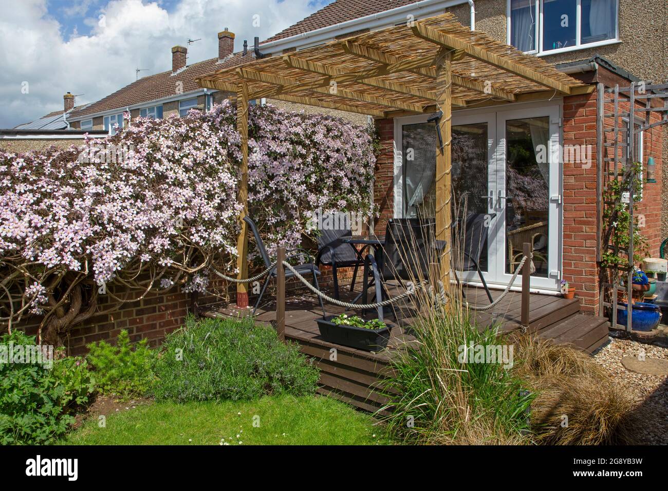 English garden with wooden decking and pergola and clematis growing along a fence Stock Photo