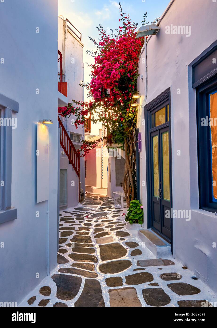 Beautiful traditional narrow cobbled alleys of Greek island towns. Whitewashed houses, shops, morning summer sunshine, bougainvillea, Mykonos, Greece. Stock Photo