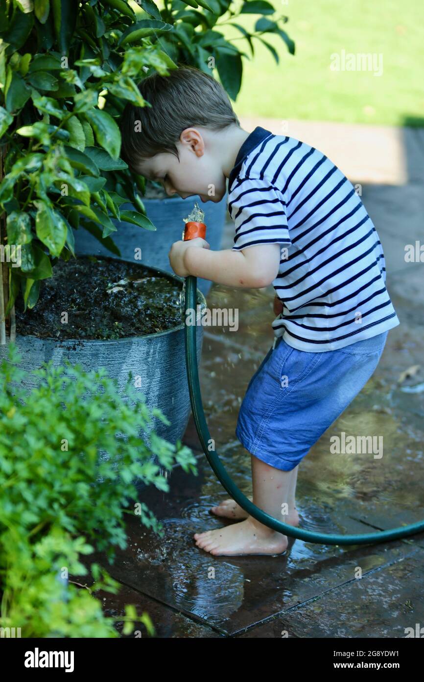 Young Australian kid drinking water from a hose while watering the