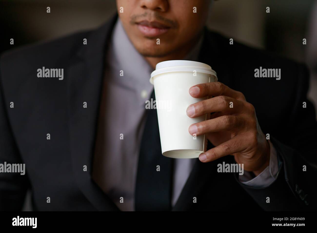 Businessman in black suit holding white paper coffee cup Stock Photo