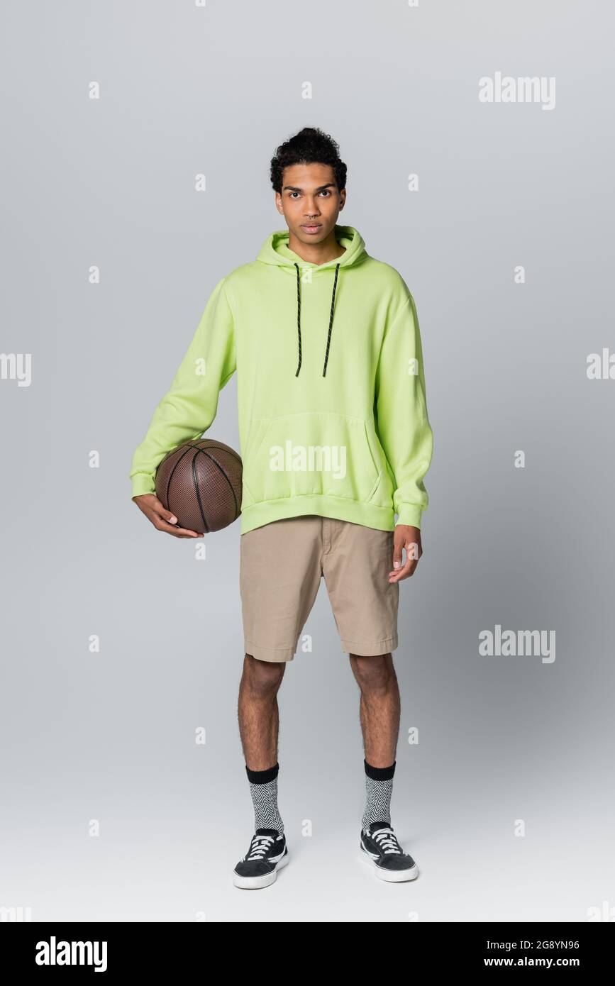 full length view of african american man in beige hoodie and green shorts holding basketball on grey background Stock Photo Alamy