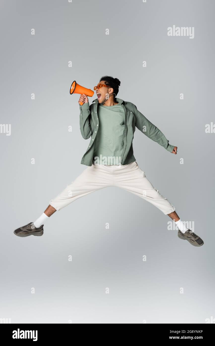 african american man in trendy clothes jumping with megaphone on grey background Stock Photo