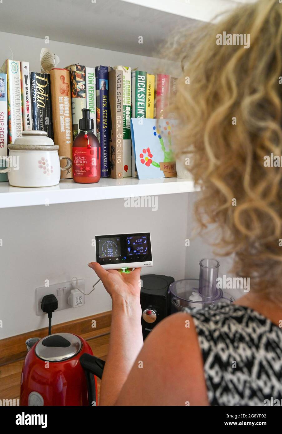 Middle aged woman looking at British Gas Smart Meter in home kitchen Stock Photo