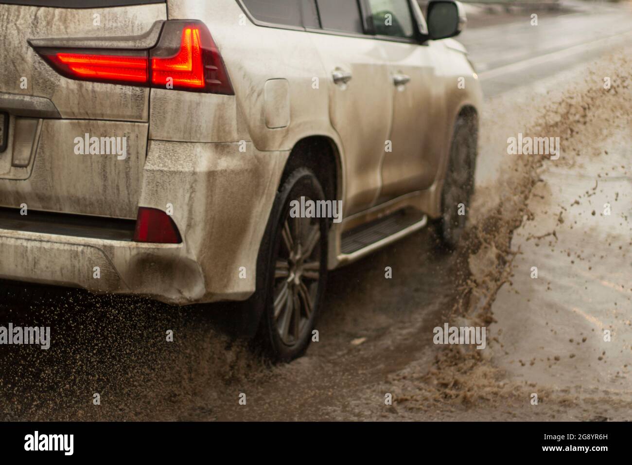The car is driving in a puddle. White car in the mud. Roads for