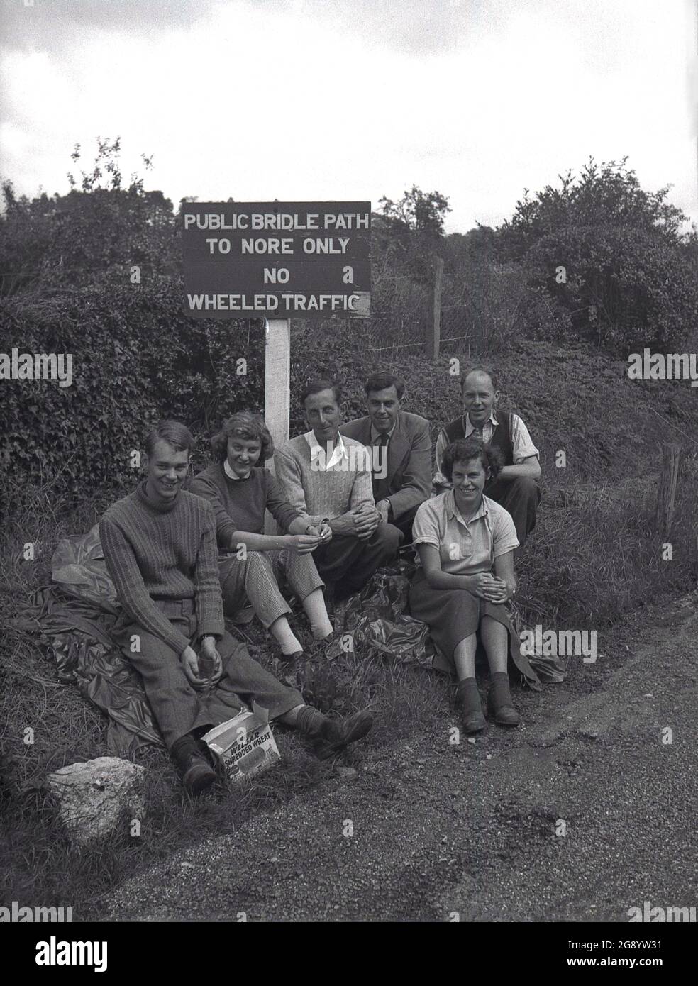 1950s, historical, outside in the countryside, a small group of people s sit for a photo by a sign for a Public Bridle Path to Nore, Kent, Engand, UK. Nore is a long bank of sand at the narrowing of the Thames Estuary and a place a walking route on the North Downs. Stock Photo