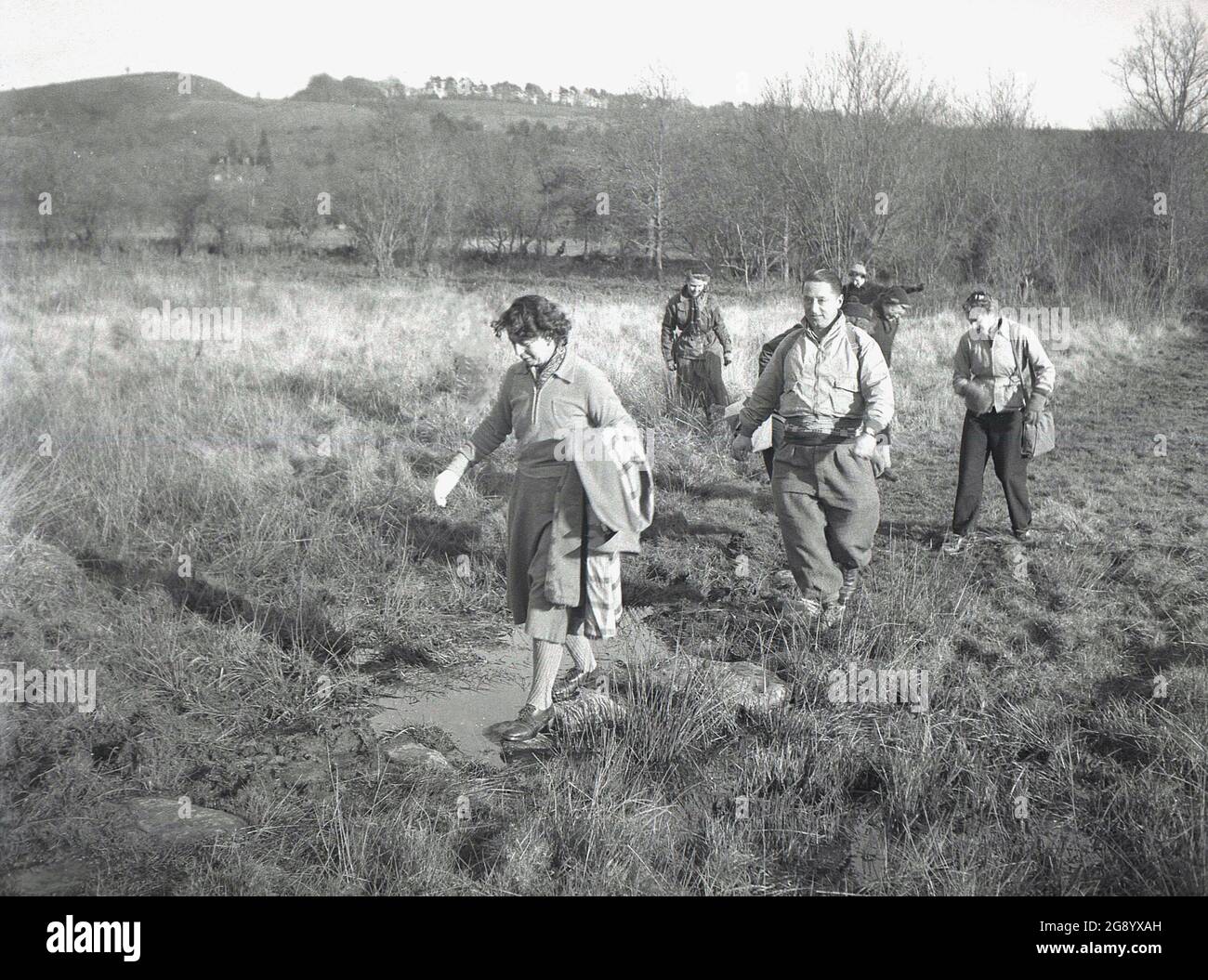 1950s, historical, people walking through a muddly path on a field near ...
