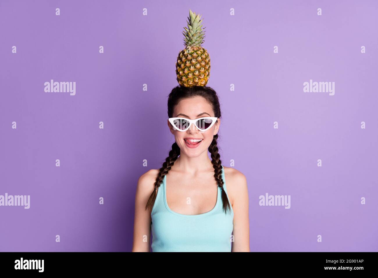 Photo portrait of young woman smiling keeping pineapple on head licking