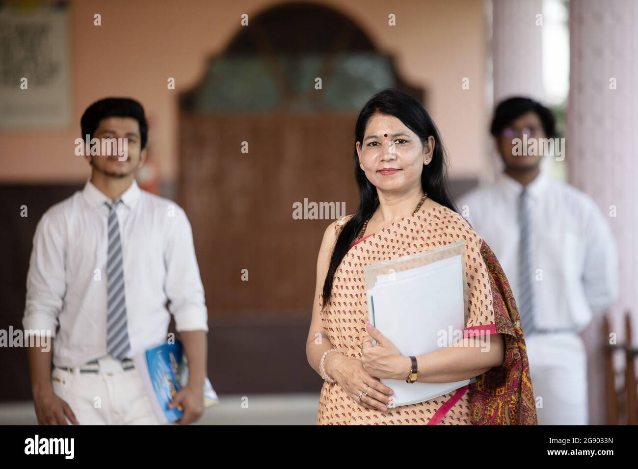 Confident smiling Indian school teacher with students in background Stock Photo