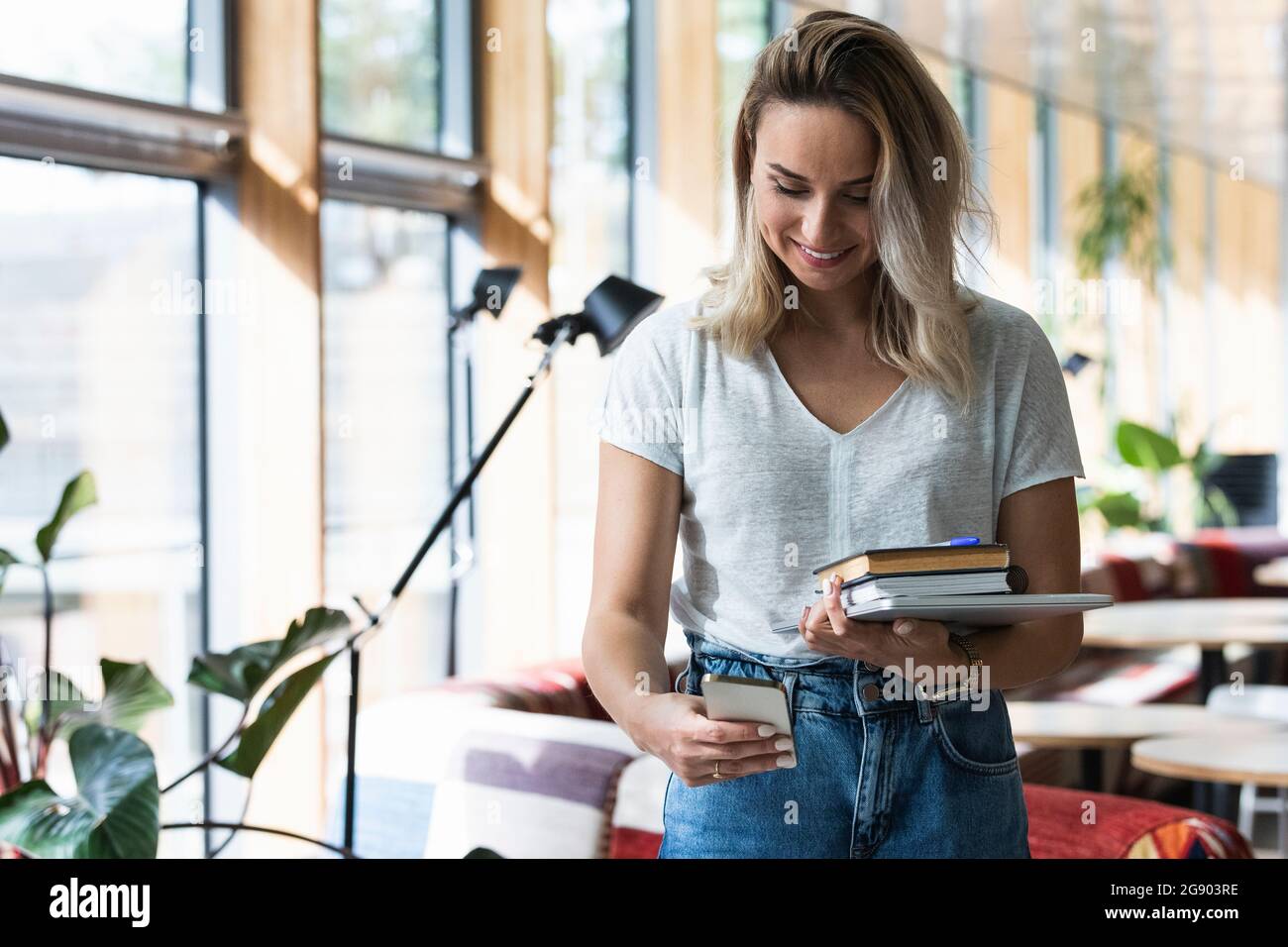 Female freelancer using phone while holding diaries and digital tablet at cafe Stock Photo