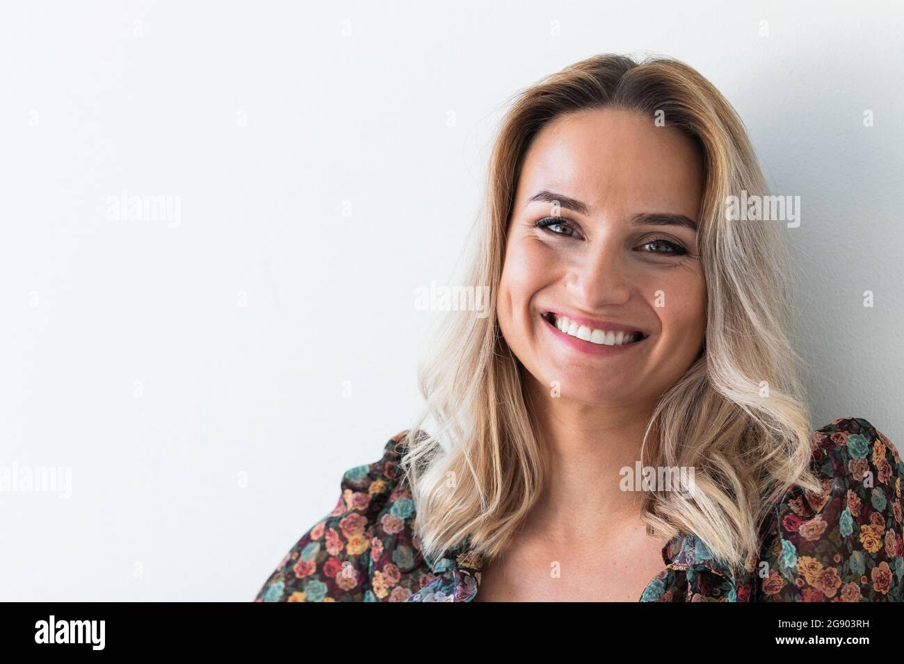 Beautiful blond woman smiling in front of white wall Stock Photo - Alamy