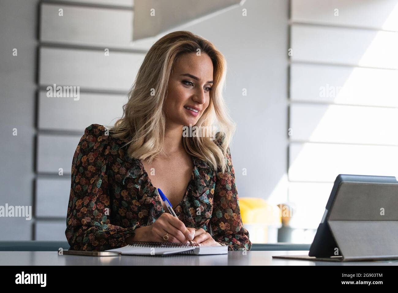 Female entrepreneur looking at digital tablet writing on diary at office Stock Photo