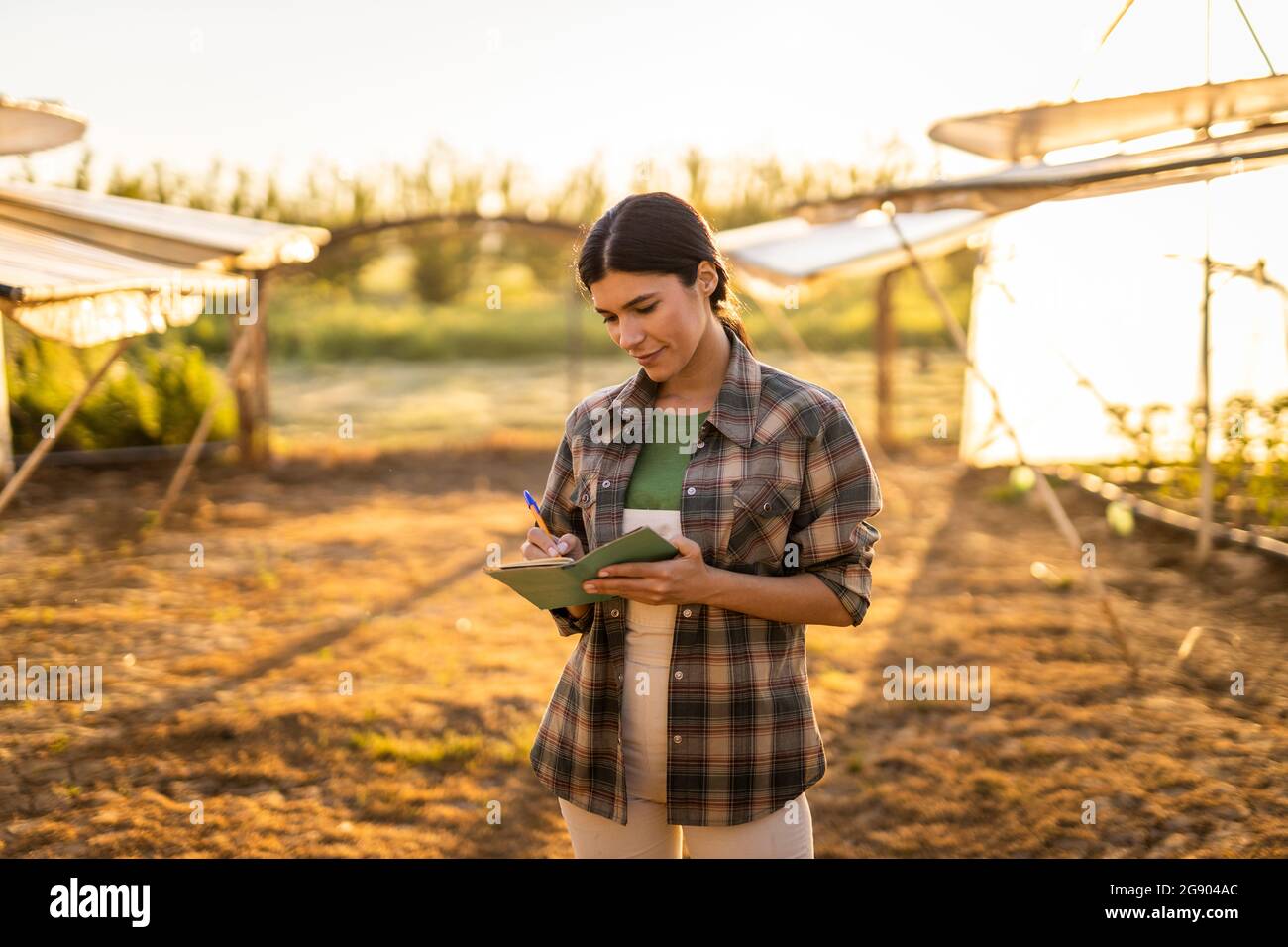 Young female farmer writing in notepad while standing at farm Stock ...
