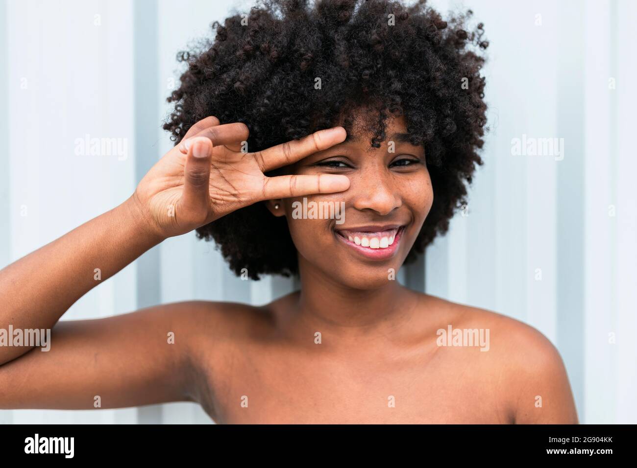 Smiling Afro woman gesturing in front of wall Stock Photo - Alamy
