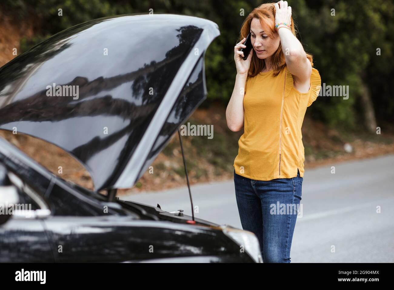 Confused woman scratching head while talking on mobile phone by car Stock Photo