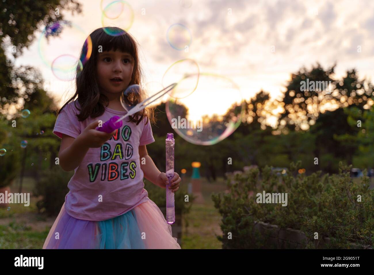 Girl looking with wand looking at soap bubbles while playing during sunset Stock Photo