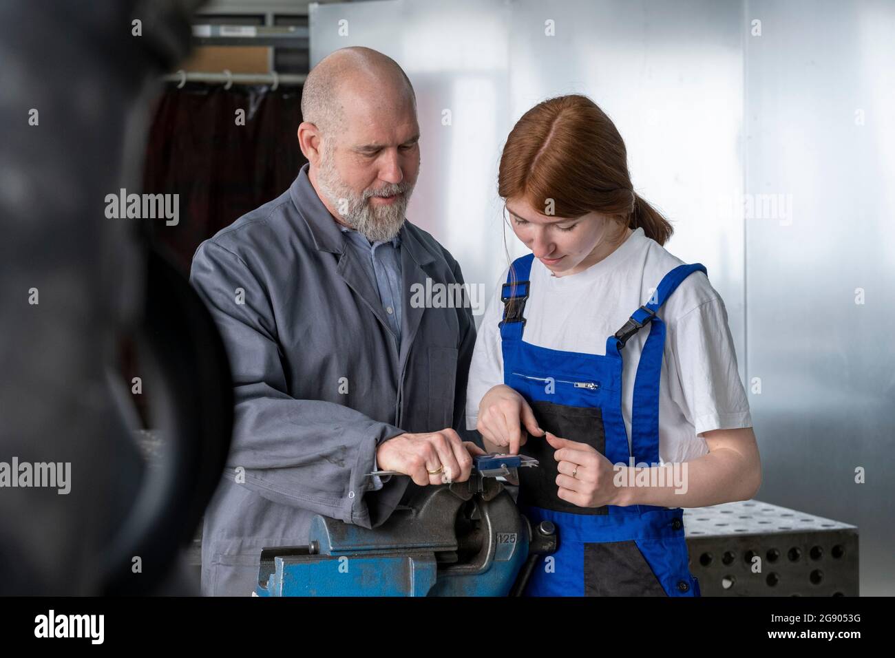 Mature instructor assisting female apprentice working in workshop Stock Photo