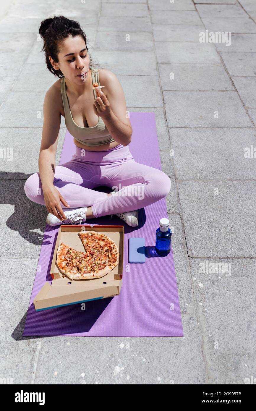 Female athlete eating pizza while sitting crosslegged on exercise mat Stock Photo Alamy