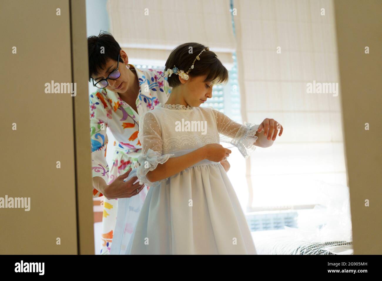 Mother helping daughter getting dressed for communion at home Stock Photo