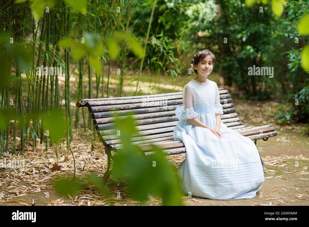 Smiling girl sitting in white dress on park bench Stock Photo