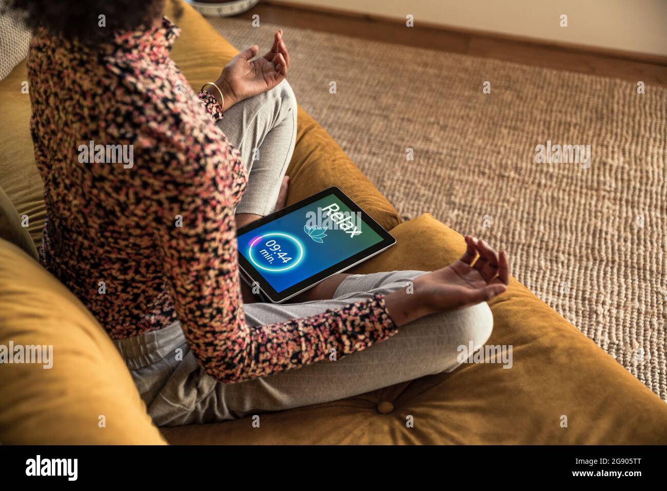 Young woman doing yoga while sitting with digital tablet on sofa Stock Photo