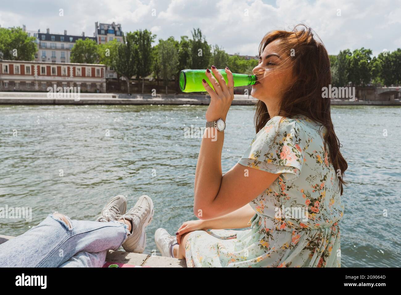 Woman drinking beer while sitting by male friend by river Stock Photo
